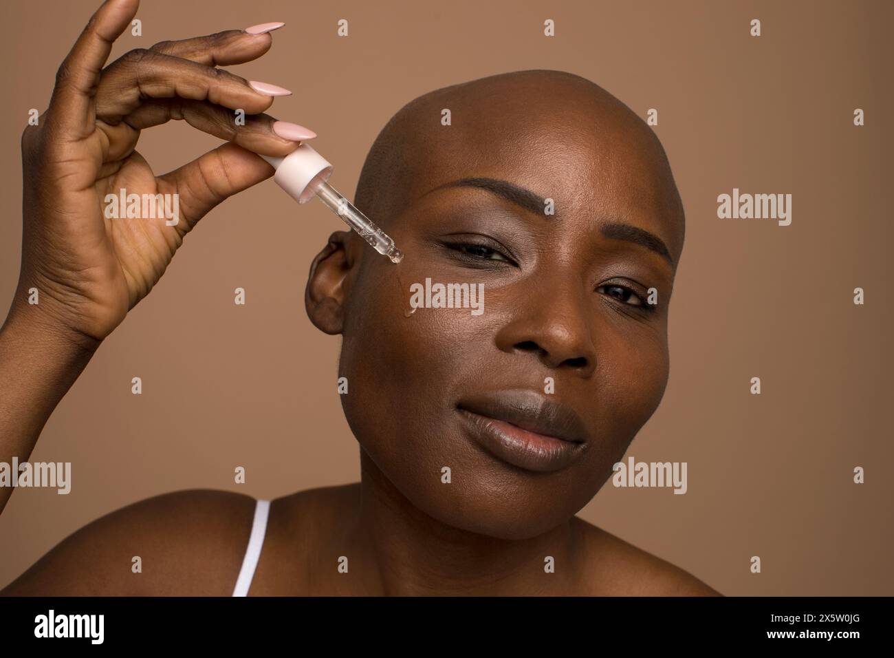 Ritratto in studio di una donna con la testa rasata che applica olio sul viso Foto Stock