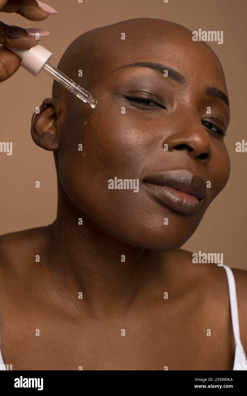 Ritratto in studio di una donna con la testa rasata che applica olio sul viso Foto Stock