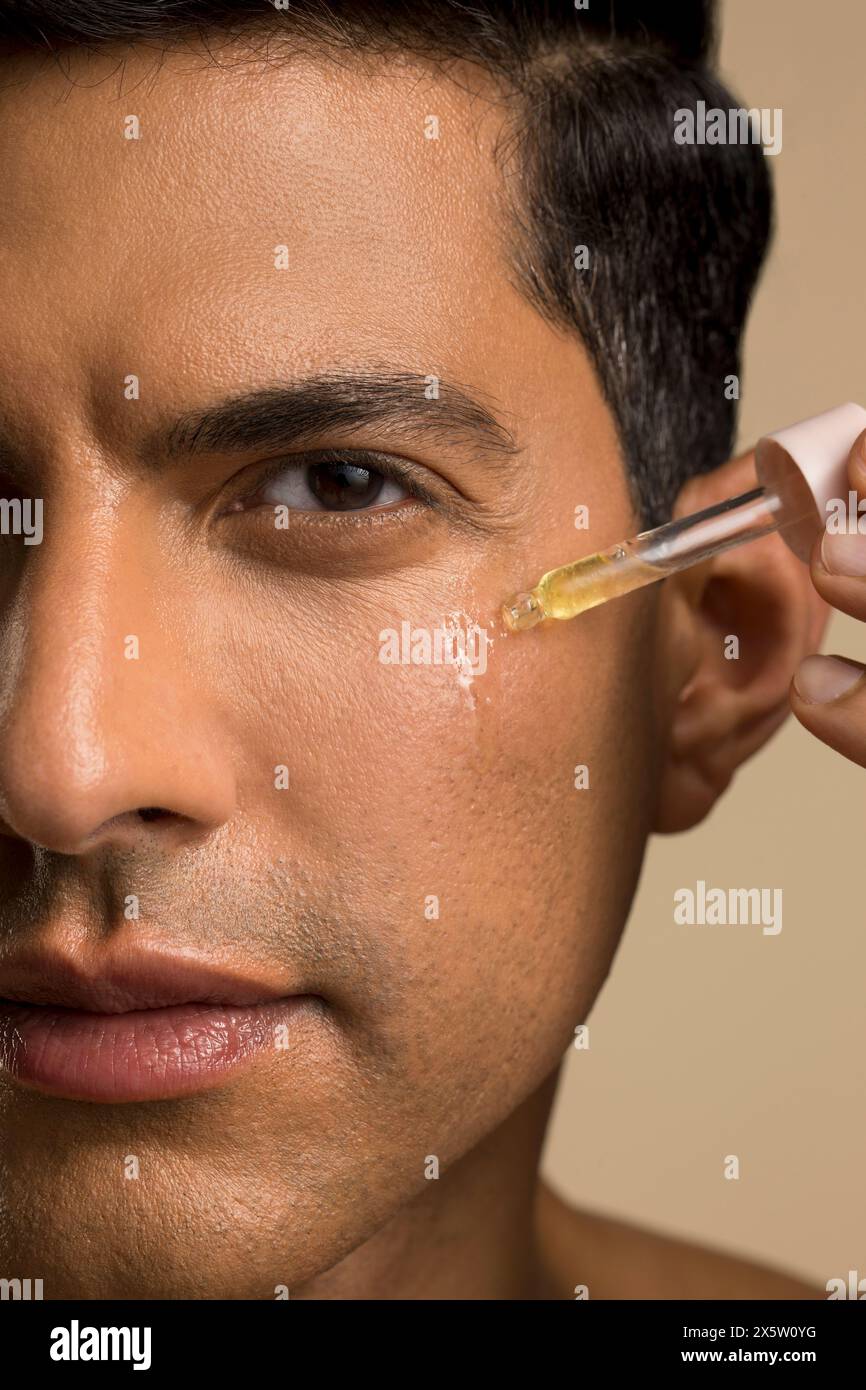 Primo piano di un uomo che applica olio sul viso Foto Stock