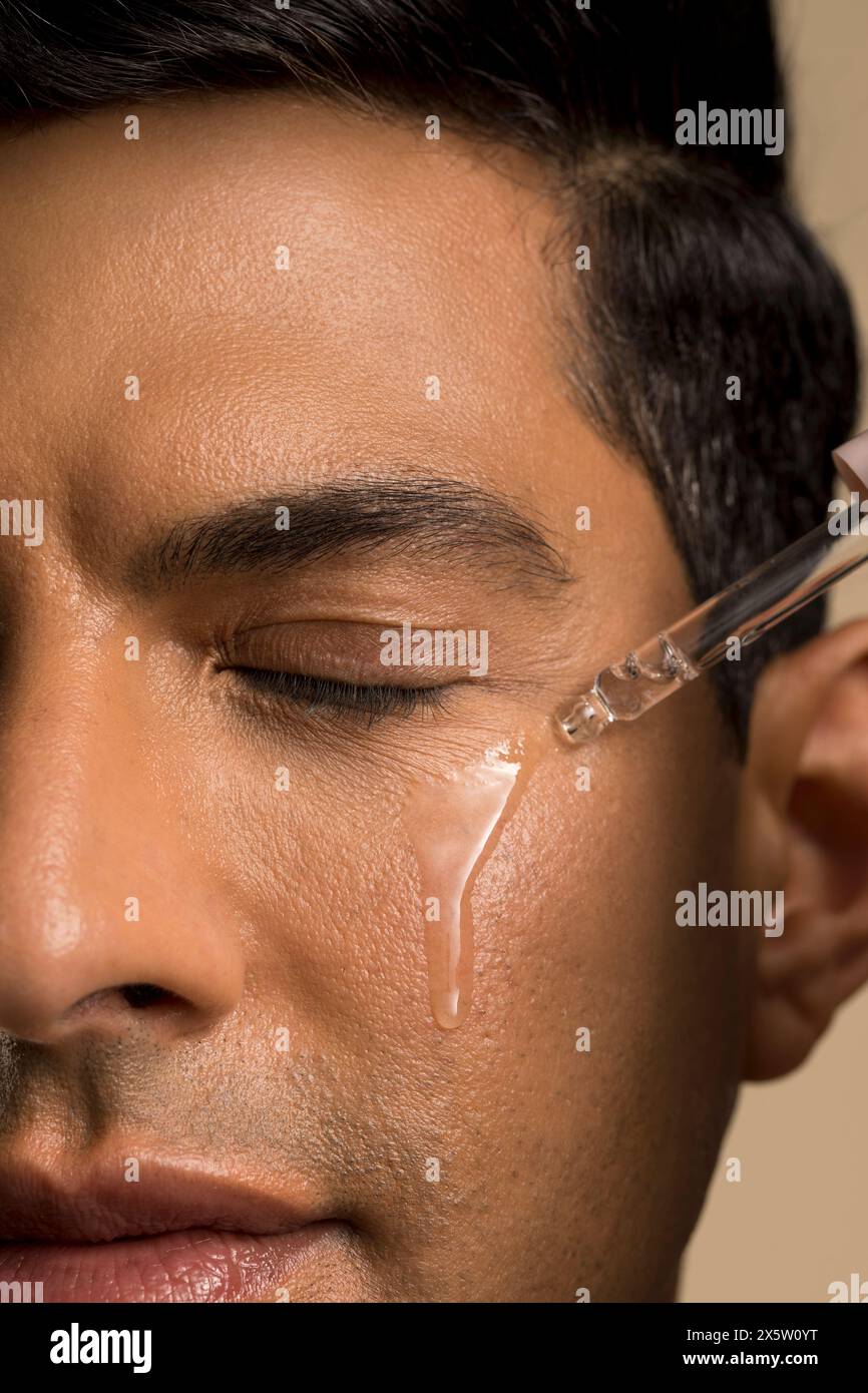 Primo piano di un uomo che applica olio sul viso Foto Stock