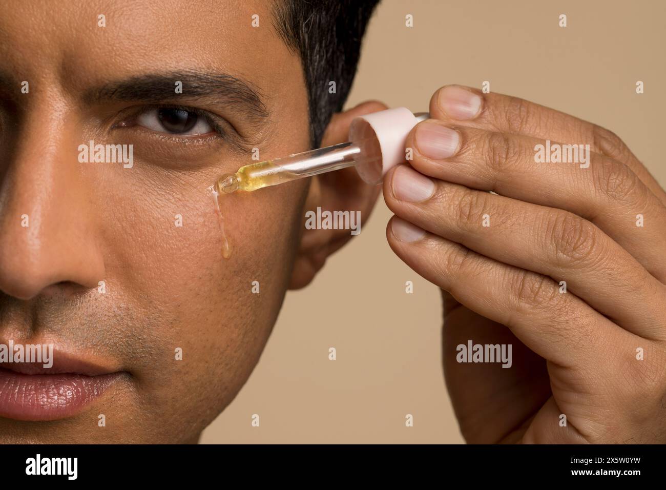 Primo piano di un uomo che applica olio sul viso Foto Stock