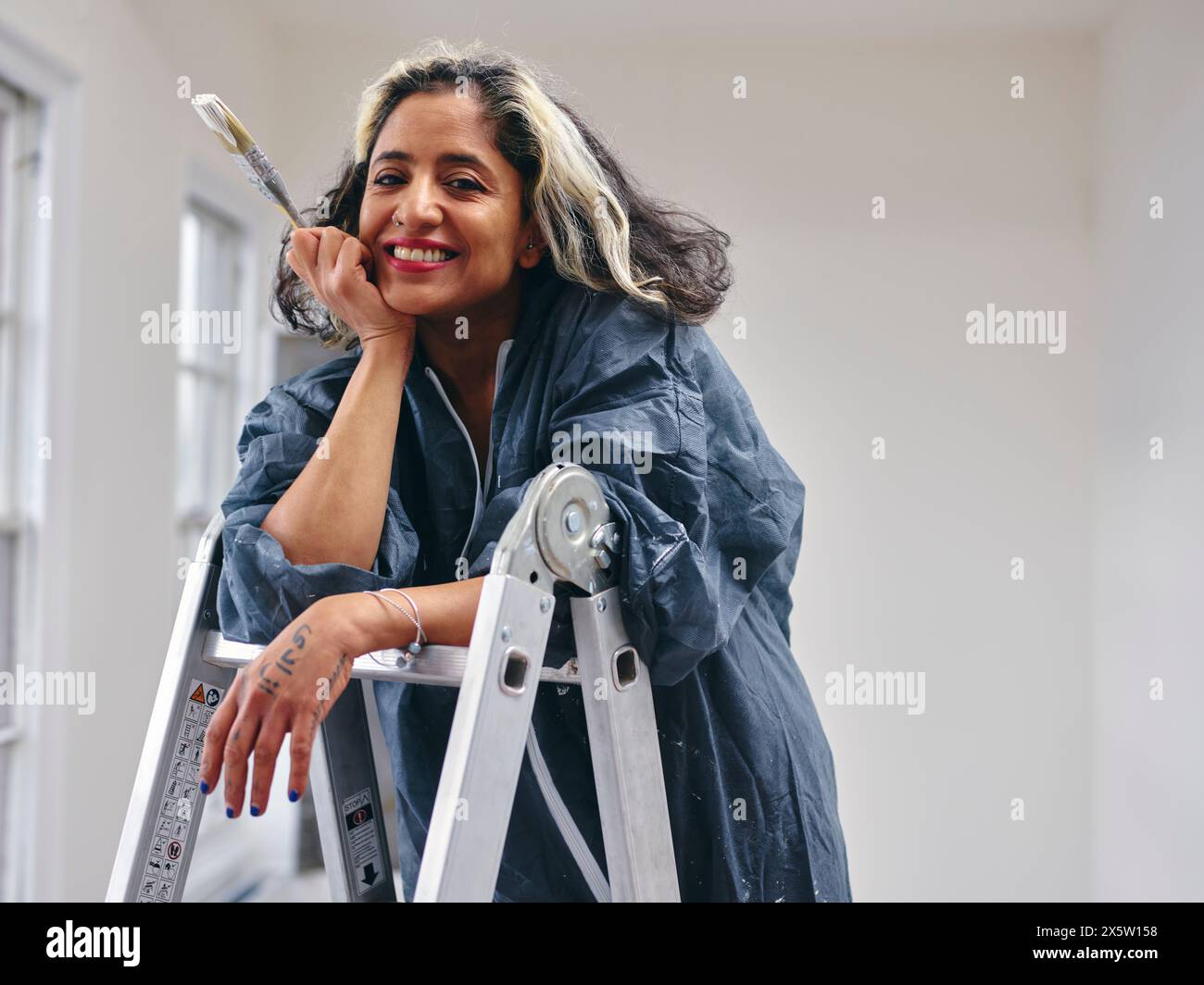 Donna sorridente in piedi sulla scala con pennello Foto Stock