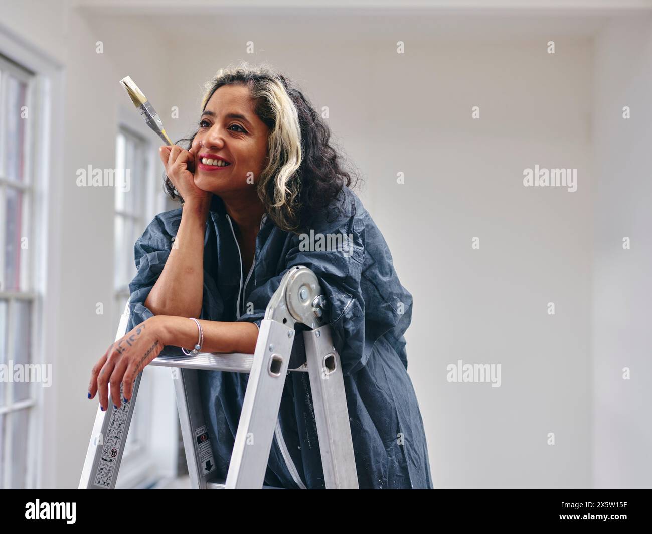 Donna sorridente in piedi sulla scala con pennello Foto Stock