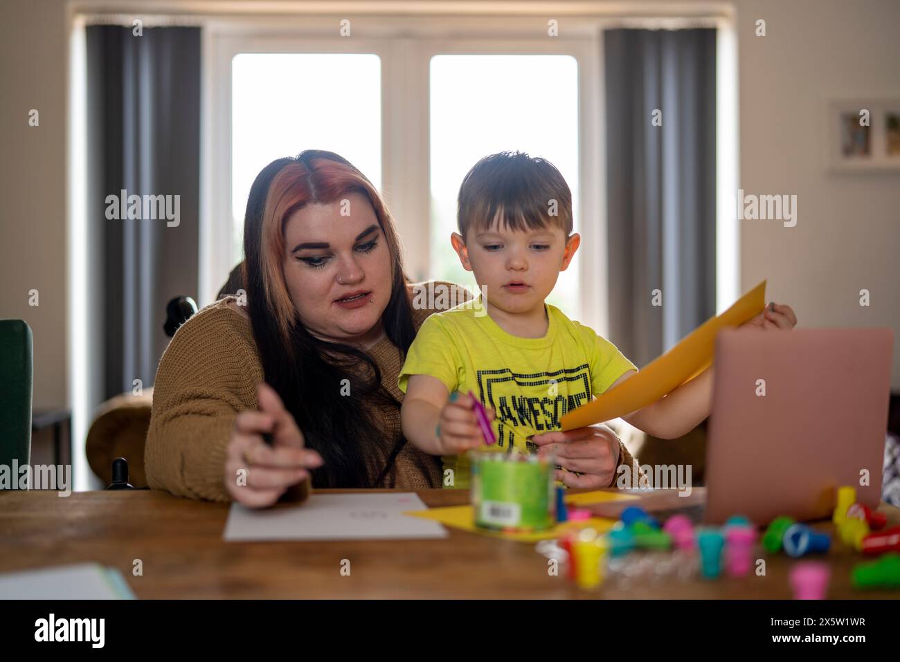 Madre in sedia a rotelle e figlio seduto a tavola e a disegnare Foto Stock