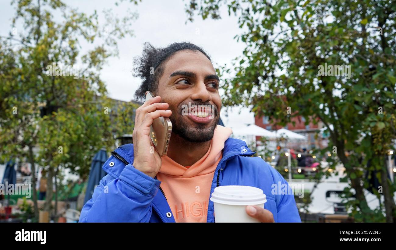 Giovane che tiene il caffè e parla al telefono Foto Stock