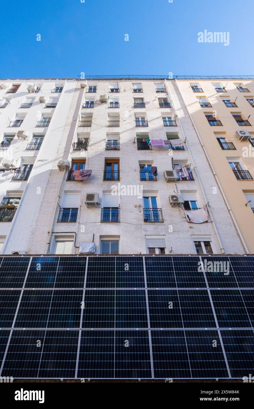 Vista frontale di un alto edificio residenziale multi-familiare dove si possono vedere i vestiti appesi. La parte inferiore è dotata di grandi pannelli solari fotovoltaici per Foto Stock