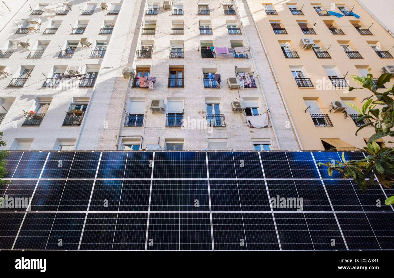 Vista frontale di un alto edificio residenziale multi-familiare dove si possono vedere i vestiti appesi. La parte inferiore è dotata di grandi pannelli solari fotovoltaici per Foto Stock