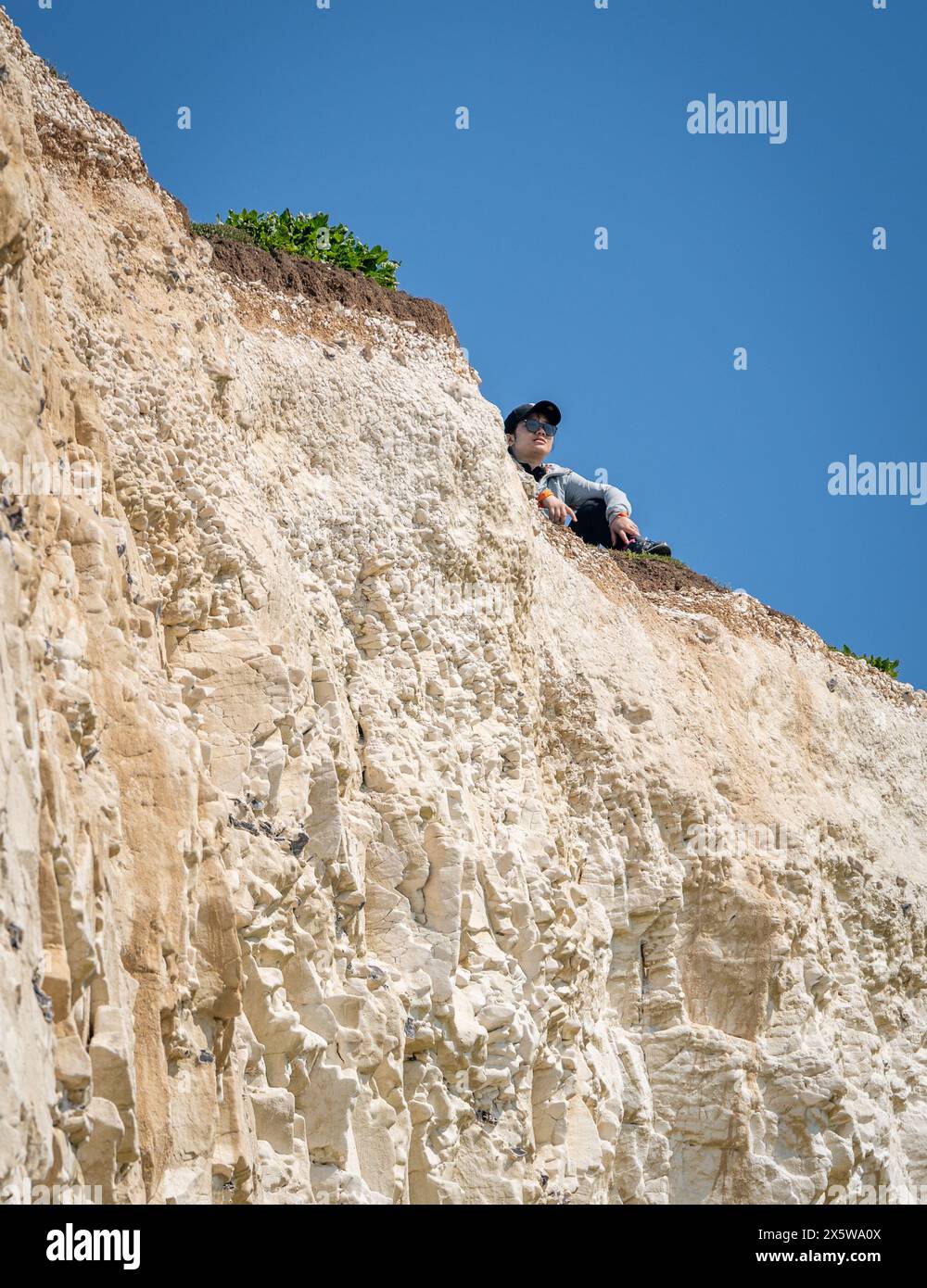 Beachy Head, East Sussex, Regno Unito. 11 maggio 2024. Un turista siede sul bordo della scogliera che si sgretola a 3oo piedi sulla costa vicino a Birling Gap, dato che si prevede che la temperatura raggiunga i 27C oggi nel weekend più caldo dell'anno finora. Beachy Head, East Sussex, UK Credit: Reppans/Alamy Live News Foto Stock