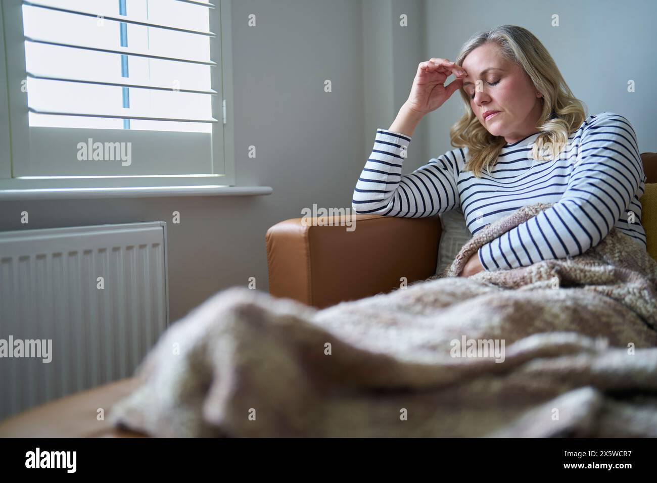 Donna matura economicamente inattiva che soffre di malattia a lungo termine seduta sul divano a casa Foto Stock