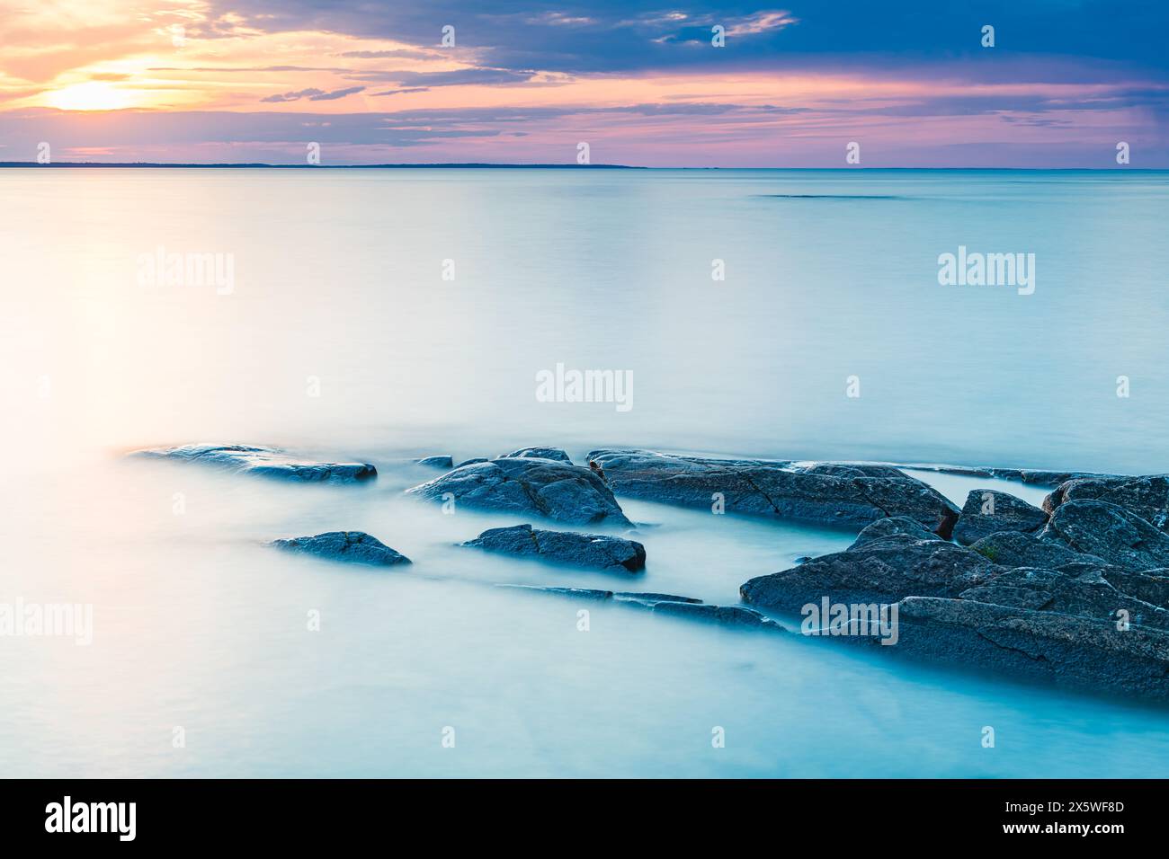 Un grande specchio d'acqua, il lago Vänern in Svezia, viene catturato durante il tramonto con rocce che ne circondano i bordi. La scena mostra il contrasto tra l'smo Foto Stock