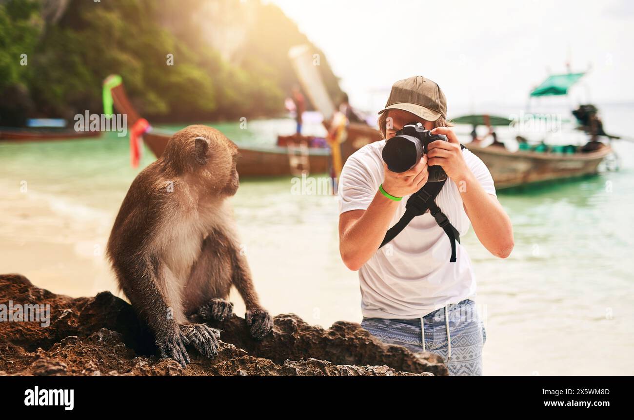 Uomo, macchina fotografica e scimmia con vacanza, spiaggia e isola tropicale con viaggio breve, Bali e turismo. Persona, fotografo e turista con attrezzatura Foto Stock