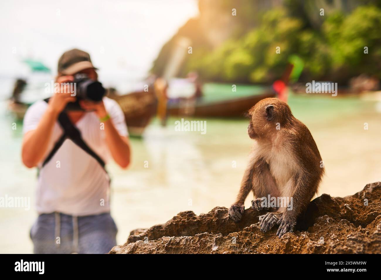 Uomo, macchina fotografica e scimmia con sole, spiaggia e isola tropicale con gita breve, Bali e mare. Persona, fotografo e turista con memoria Foto Stock