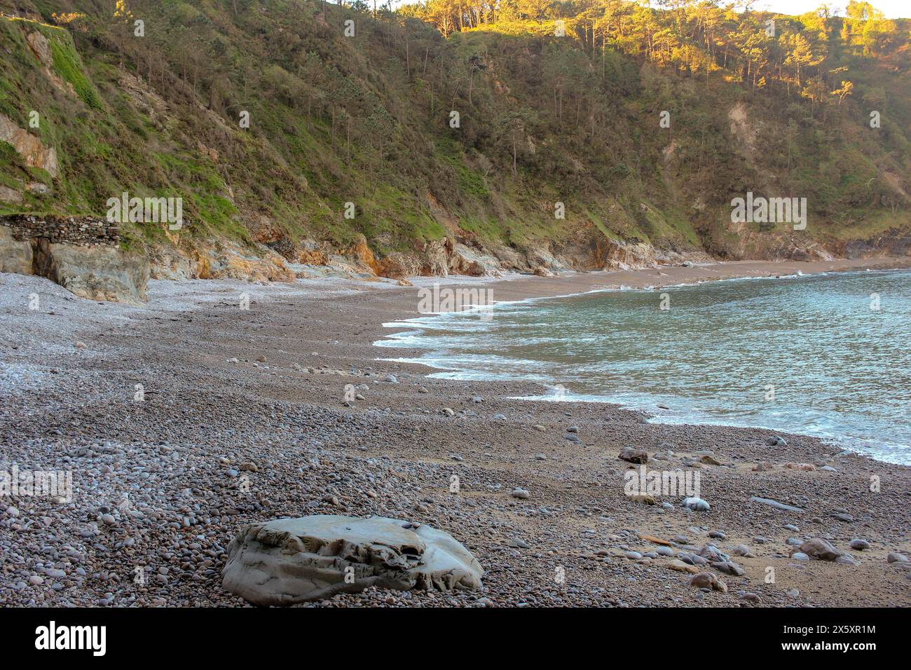 Piccole onde che raggiungono la spiaggia di Silence, una spiaggia piena di piccole pietre nel nord della Spagna Foto Stock
