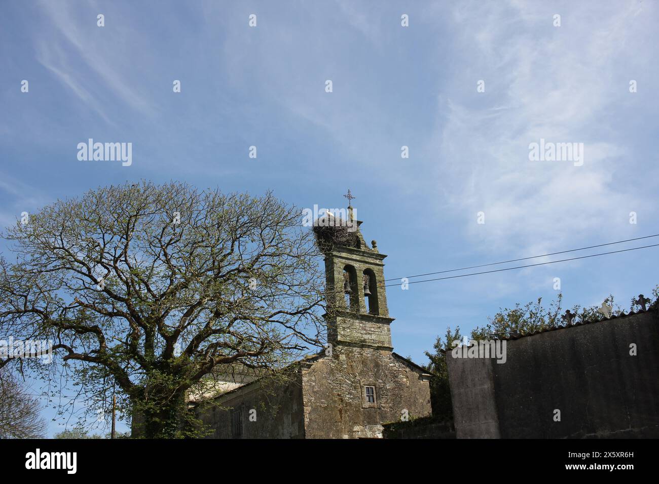 la cicogna nidifica in una cappella in Galizia, Spagna, sotto un cielo blu e bianco Foto Stock