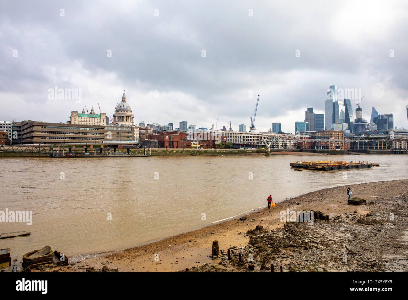 Il Tamigi con la bassa marea nel centro di Londra con persone che camminano lungo il letto del fiume, i grattacieli della città di Londra e la cattedrale di St Pauls, Inghilterra, Regno Unito Foto Stock