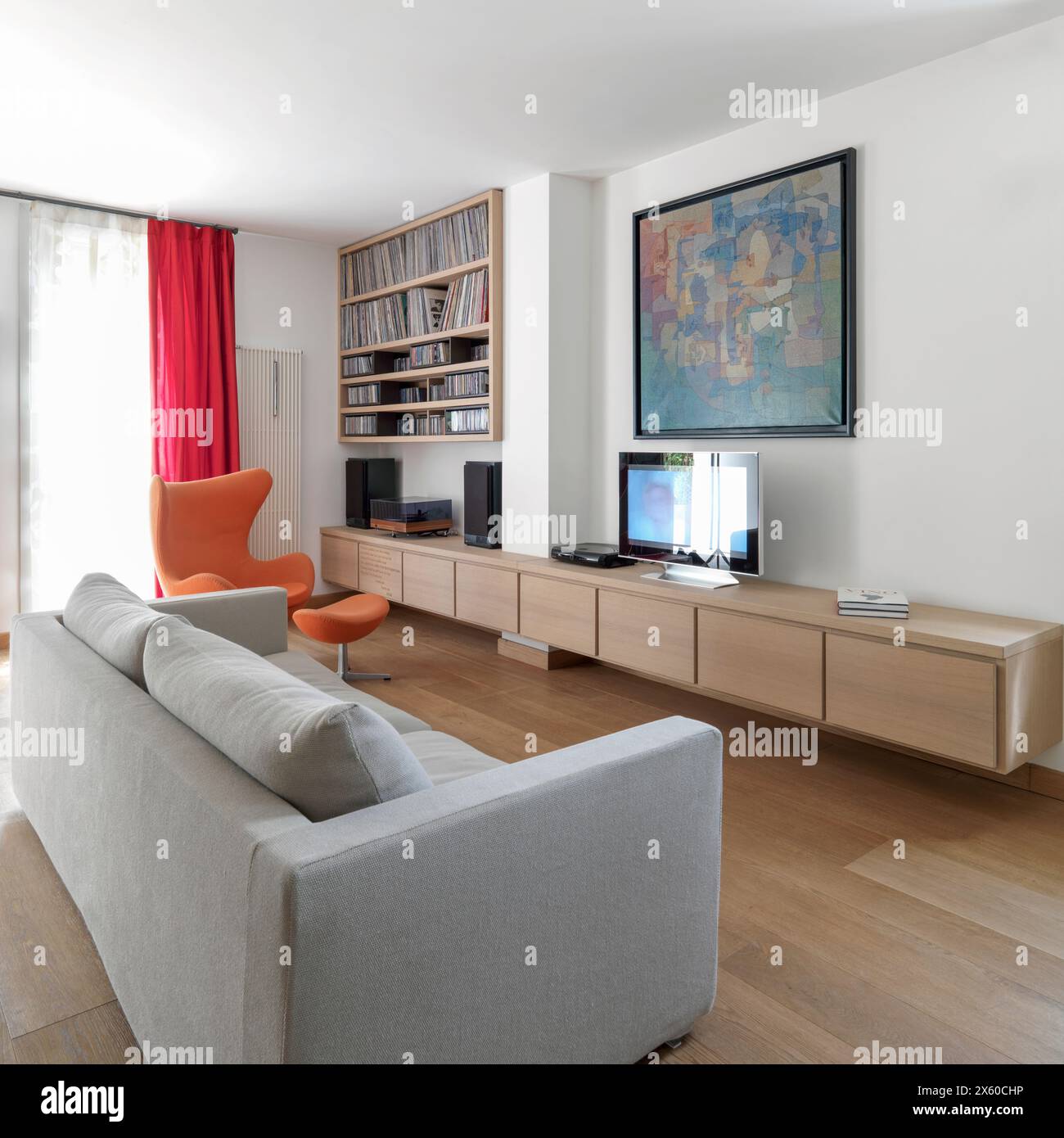 Immagine interna di un moderno soggiorno con divano in tessuto e mobili in legno in primo piano, poltrone e libreria sullo sfondo Foto Stock