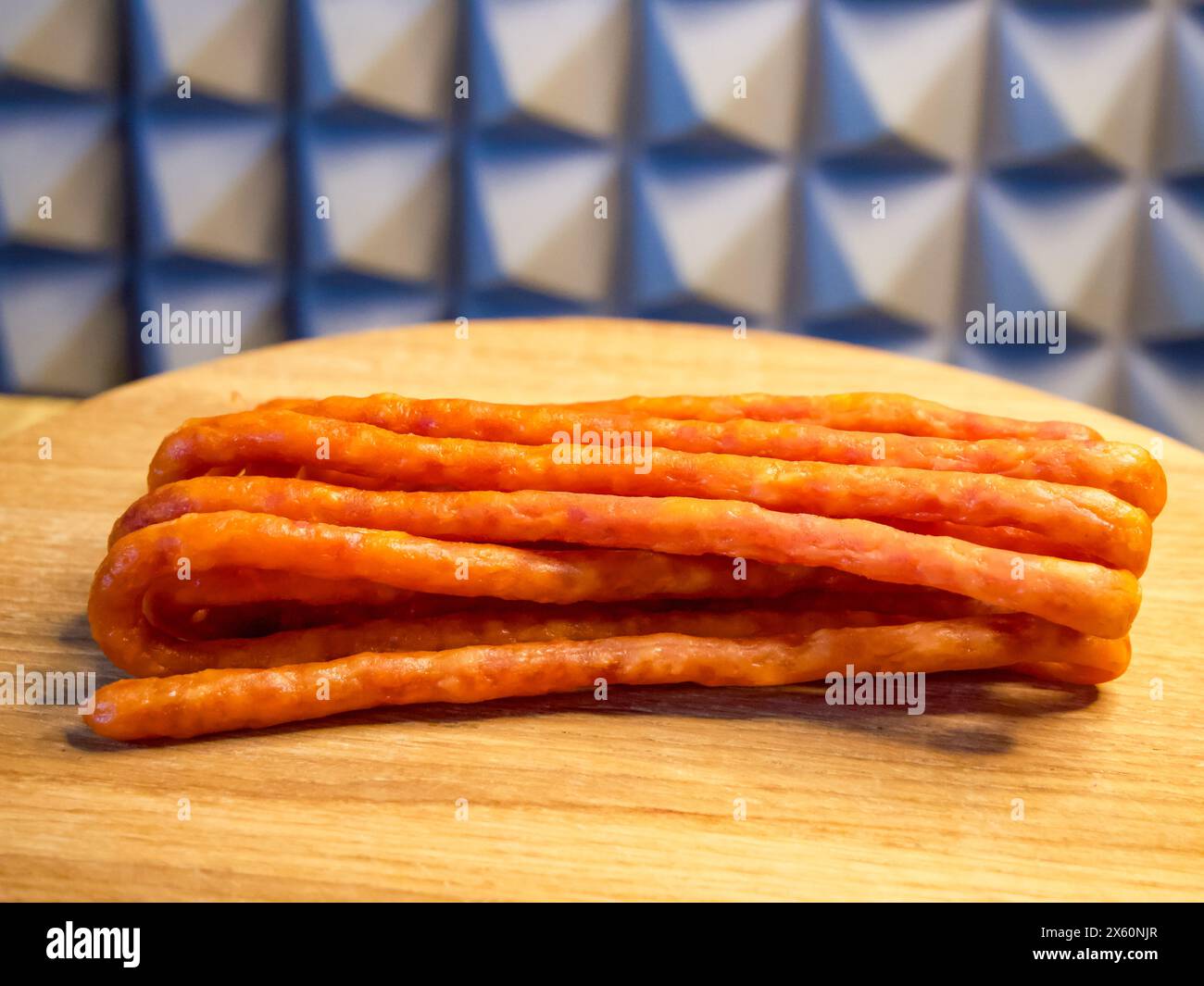 Salsicce ammassate su una superficie in legno, in contrasto con uno sfondo a scacchi. Ideale per presentazioni culinarie o promozioni per negozi di alimentari. Foto Stock