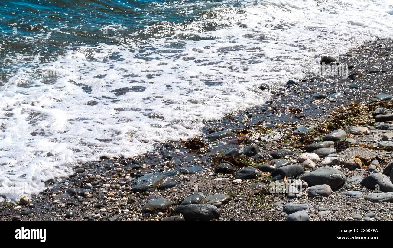 Le onde oceaniche si infrangono contro le rocce, creando una scena bella e serena. L'acqua è di colore blu intenso e le rocce sono sparse Foto Stock