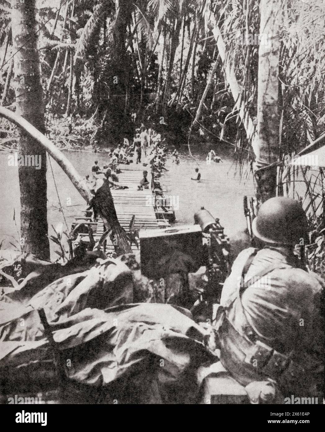 Soldati alleati che costruiscono un ponte nel Pacifico meridionale durante la ritirata giapponese in nuova Guinea. Un mitragliere tiene d'occhio le pattuglie e i cecchini giapponesi, ottobre 1943. Da The War in Pictures, Fifth Year. Foto Stock