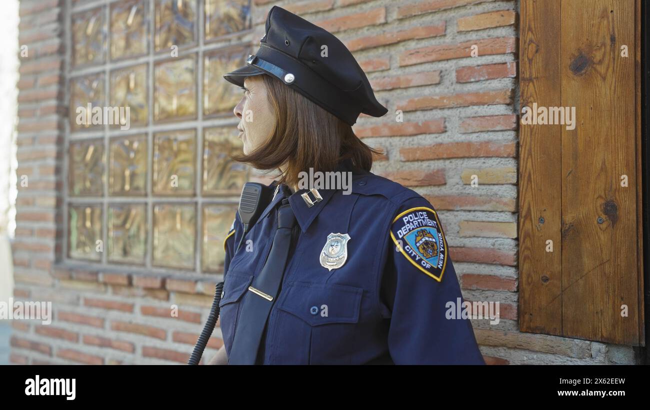 Una donna matura ufficiale sta accanto a un muro di mattoni, simboleggiando le forze dell'ordine in un ambiente urbano. Foto Stock