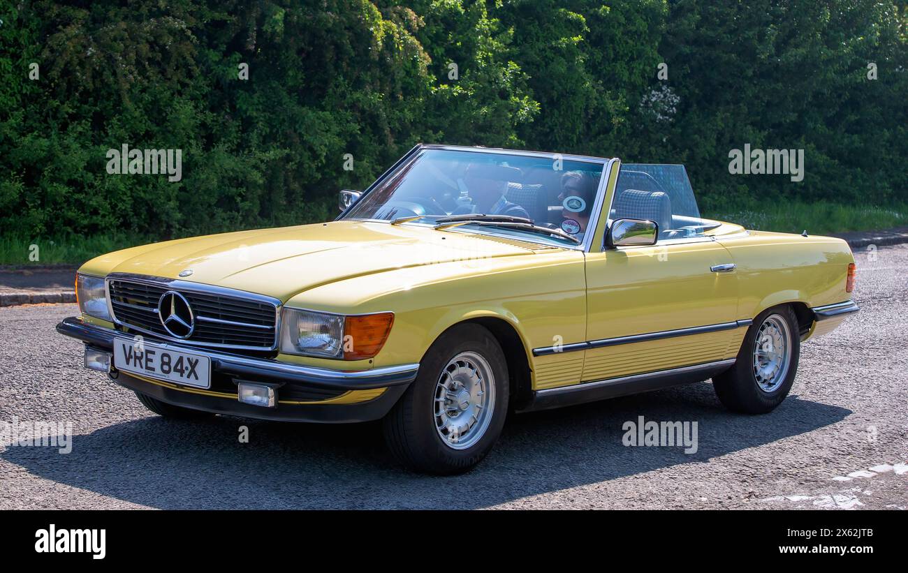 Stoke Goldington, Regno Unito - 12 maggio 2024:1982 Mercedes Benz SL classica gialla che guida su una strada britannica Foto Stock