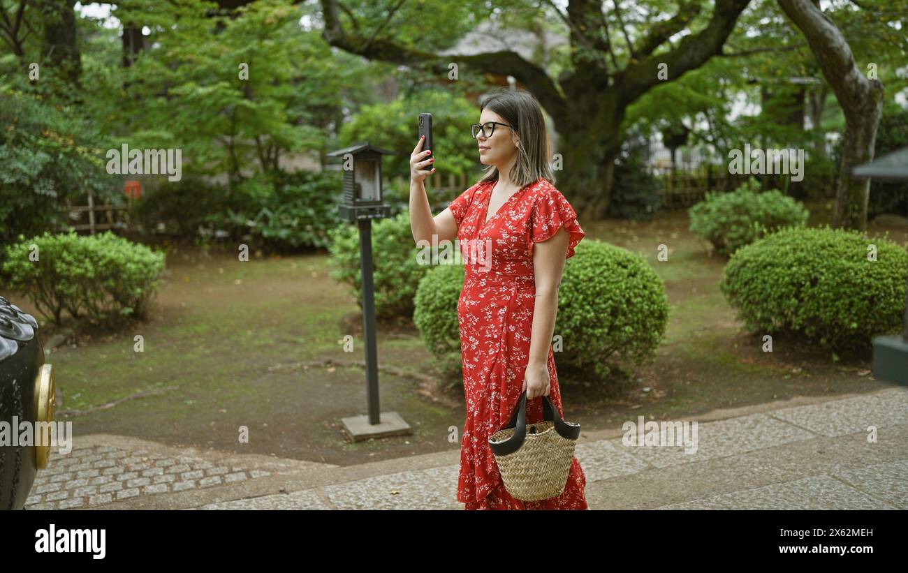 La donna ispanica con gli occhiali cattura l'antica bellezza del tempio gotokuji del giappone con il suo telefono, godendosi il suo ruolo di turista Foto Stock