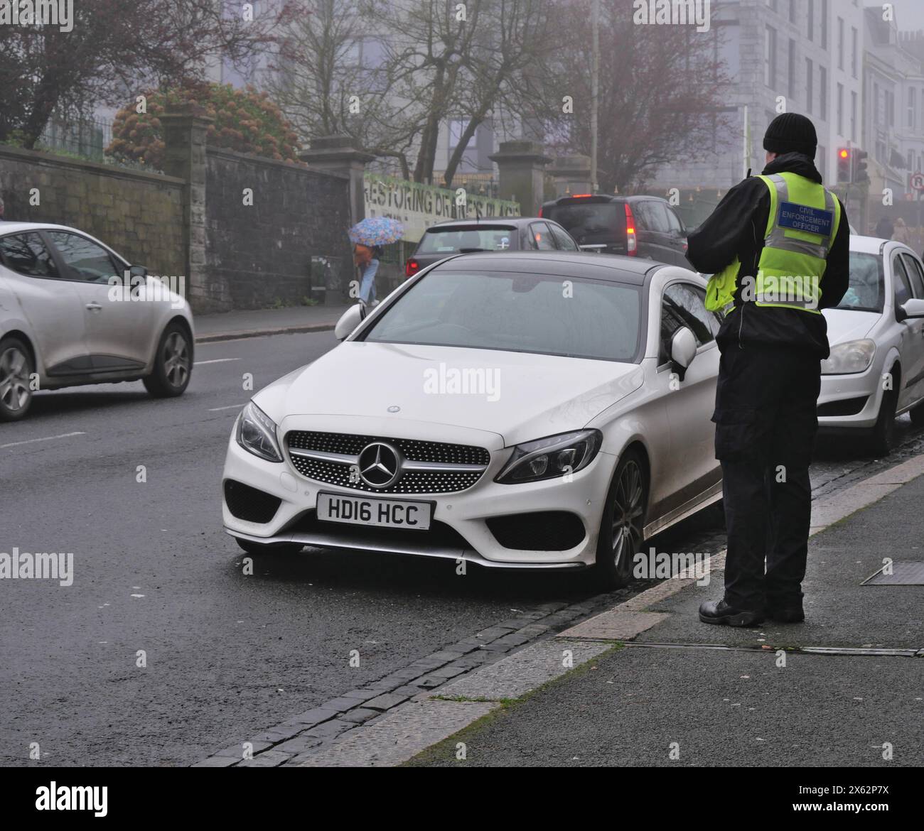 Un funzionario delle forze dell'ordine, un responsabile del parcheggio, controllare le auto parcheggiate in una trafficata strada del centro città. Plymouth, Regno Unito Foto Stock