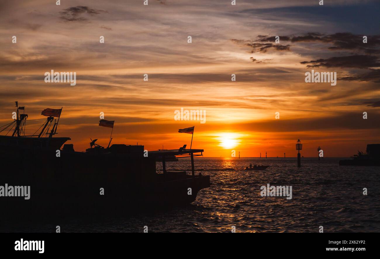 Silhuettes di barche da pesca con bandiere malesi ormeggiate al mercato del pesce KK al tramonto Foto Stock