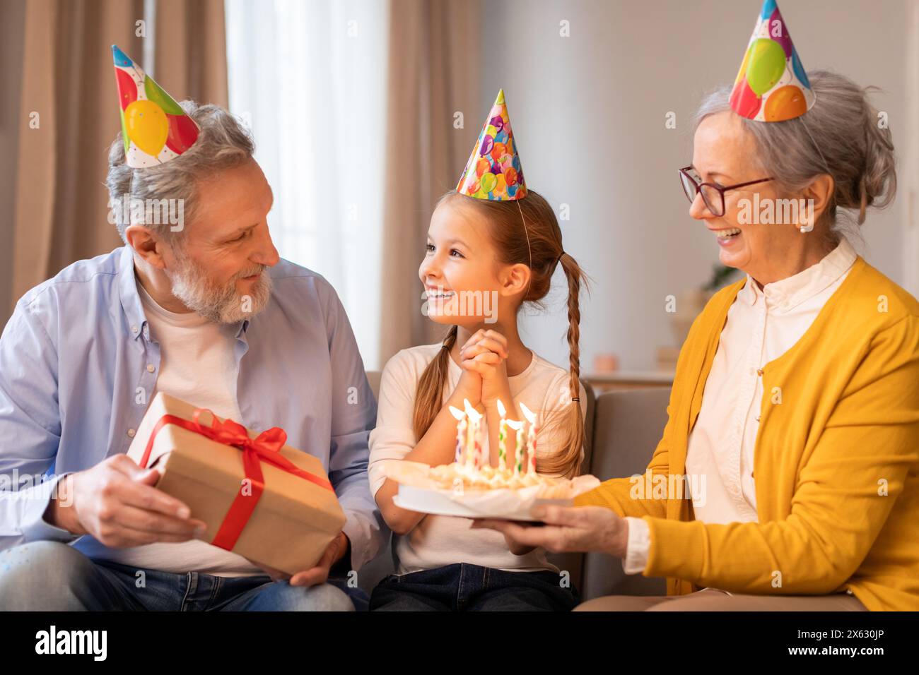 I nonni celebrano il compleanno delle ragazze con torta e regalo al chiuso Foto Stock