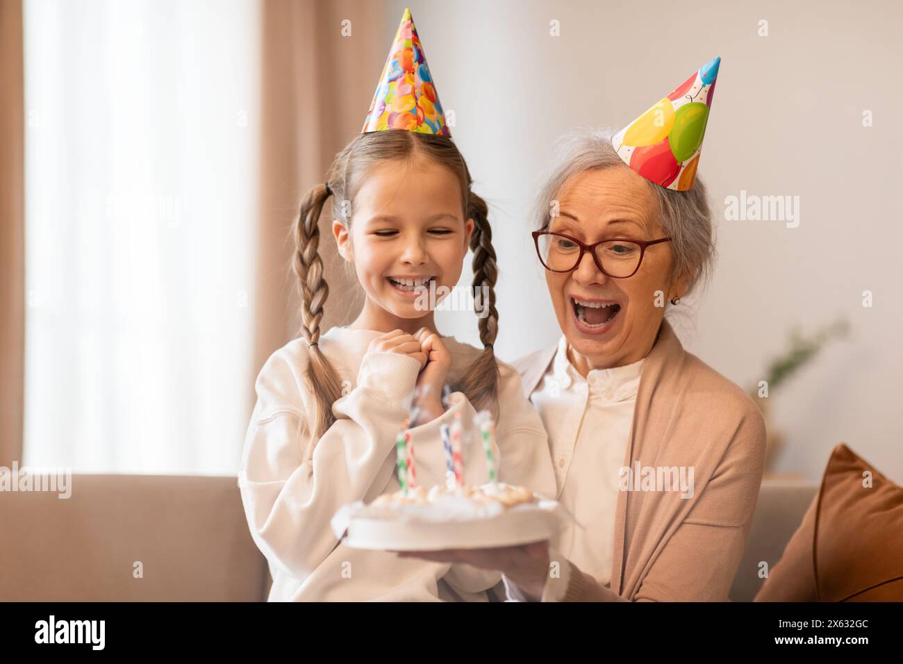 Donna più anziana e ragazza che indossa cappelli di compleanno Foto Stock