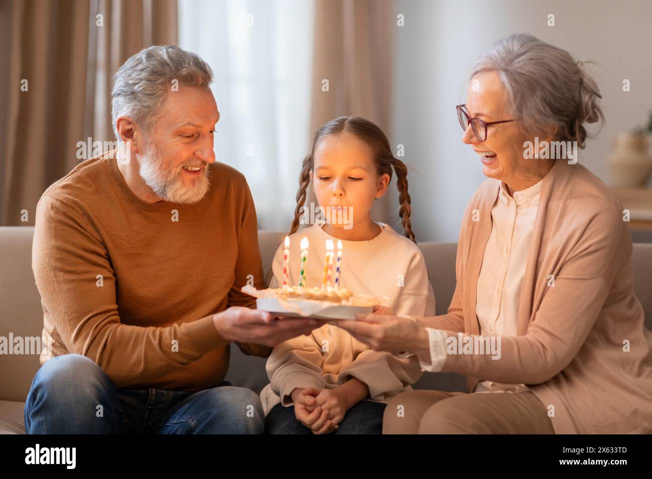 I nonni celebrano il compleanno delle ragazze con torta e candele al chiuso Foto Stock