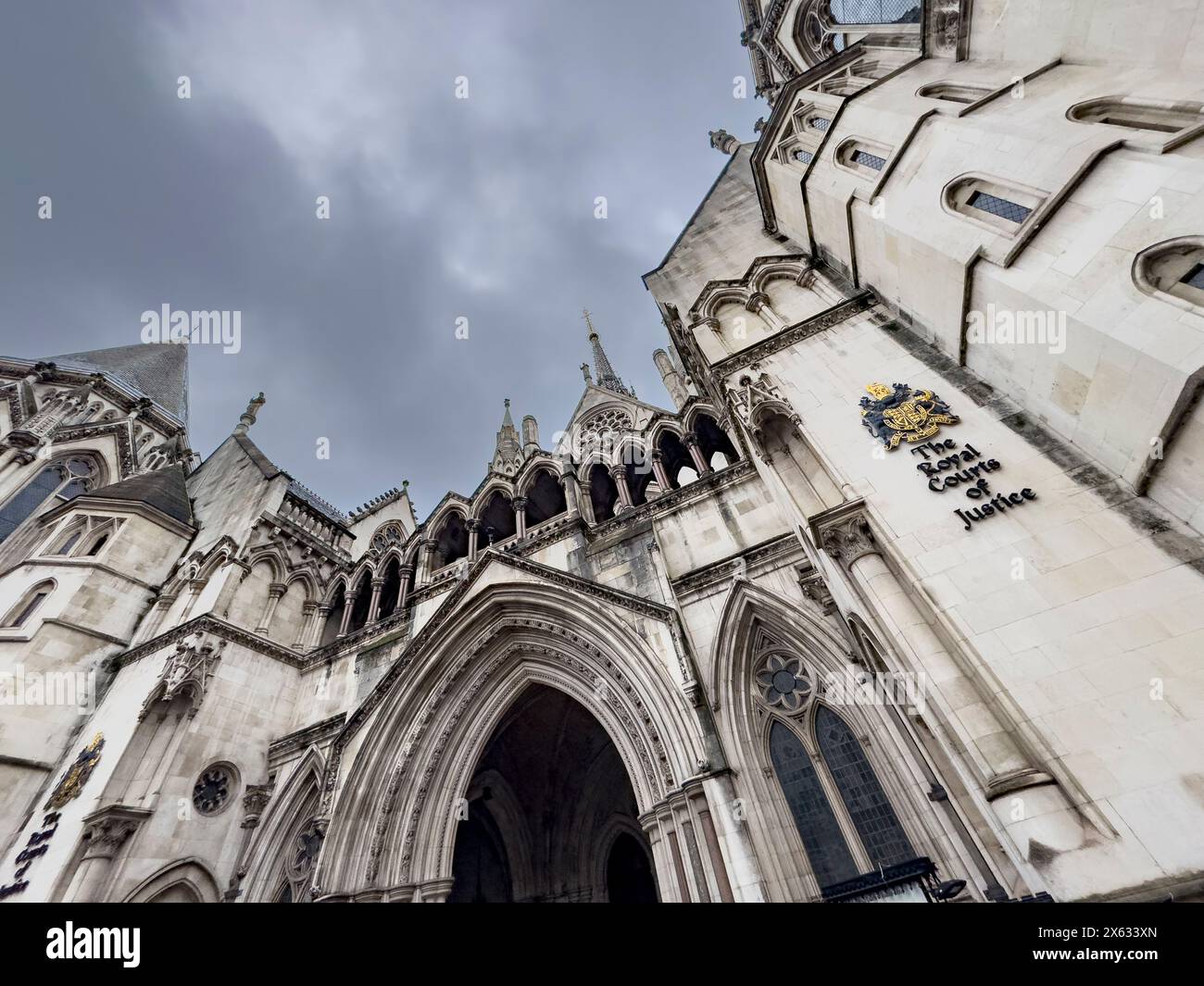 Vista esterna della Royal Courts of Justice di Londra, catturata da un'angolazione bassa contro un drammatico cielo grigio. Foto Stock