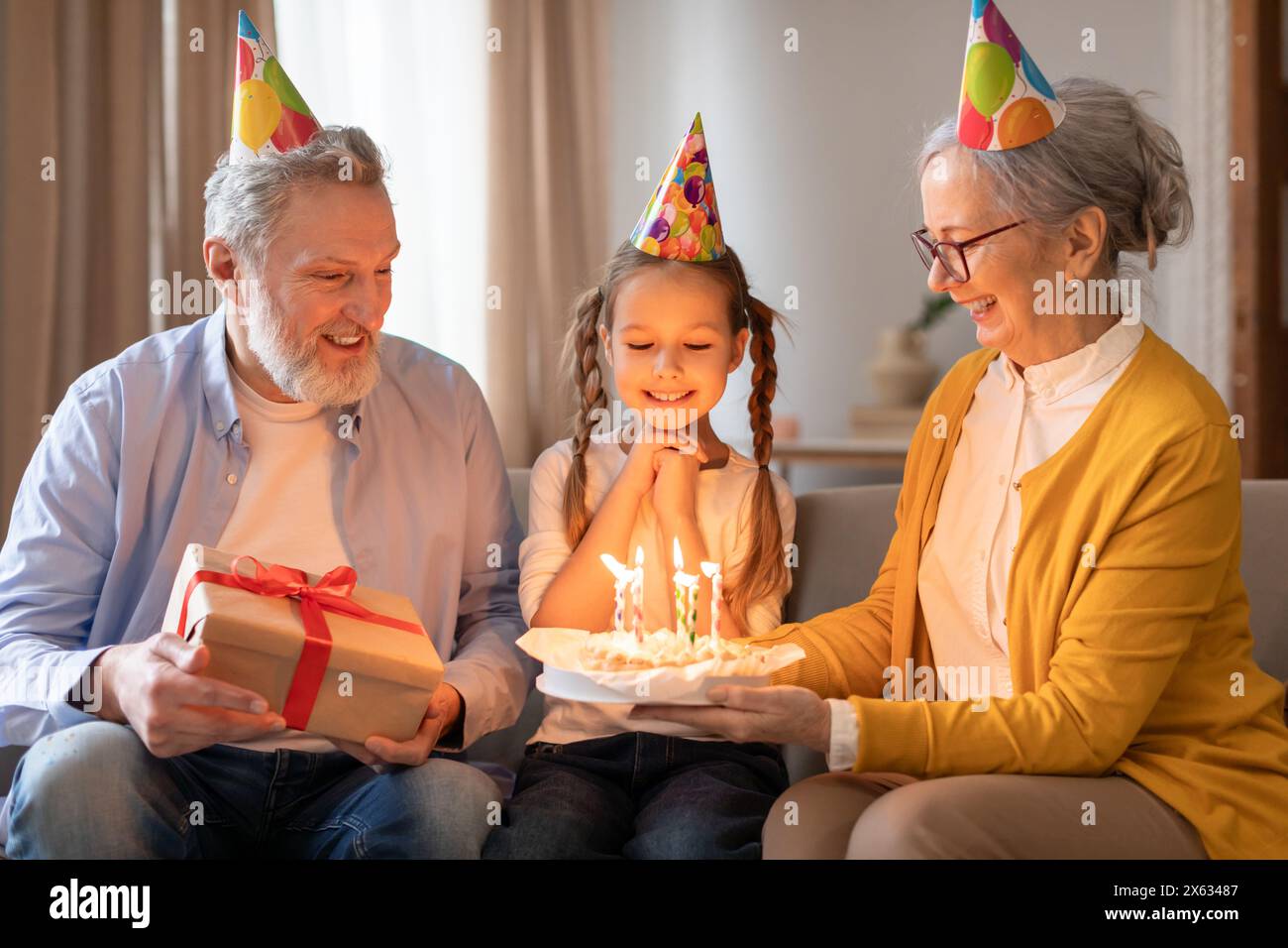 La nipote celebra il compleanno con i nonni premurosi nell'accogliente soggiorno Foto Stock