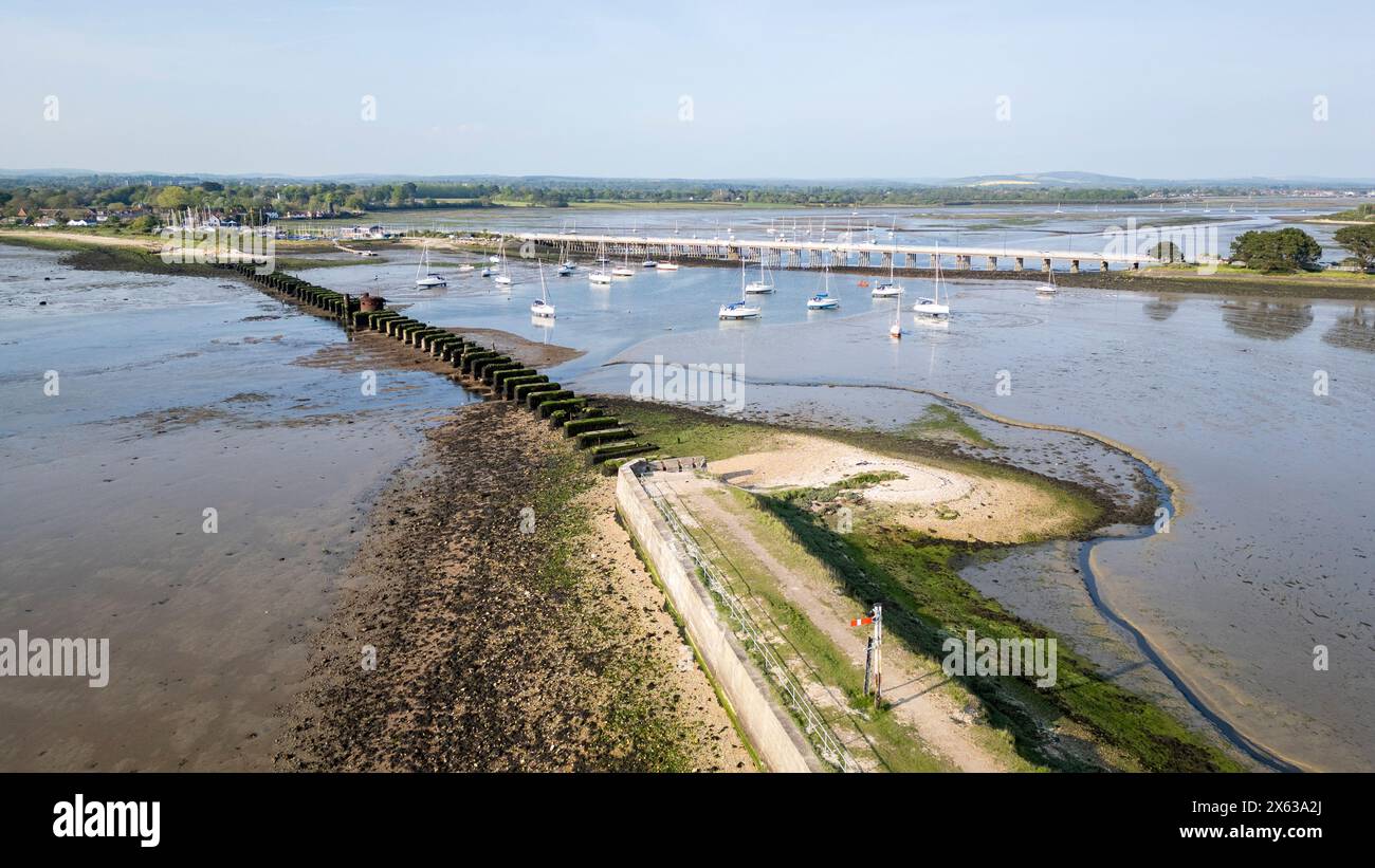 Resti del vecchio ponte ferroviario tra Langstone (in cima alla foto) e Hayling Island nell'Hampshire, Regno Unito, con un ponte stradale dietro Foto Stock