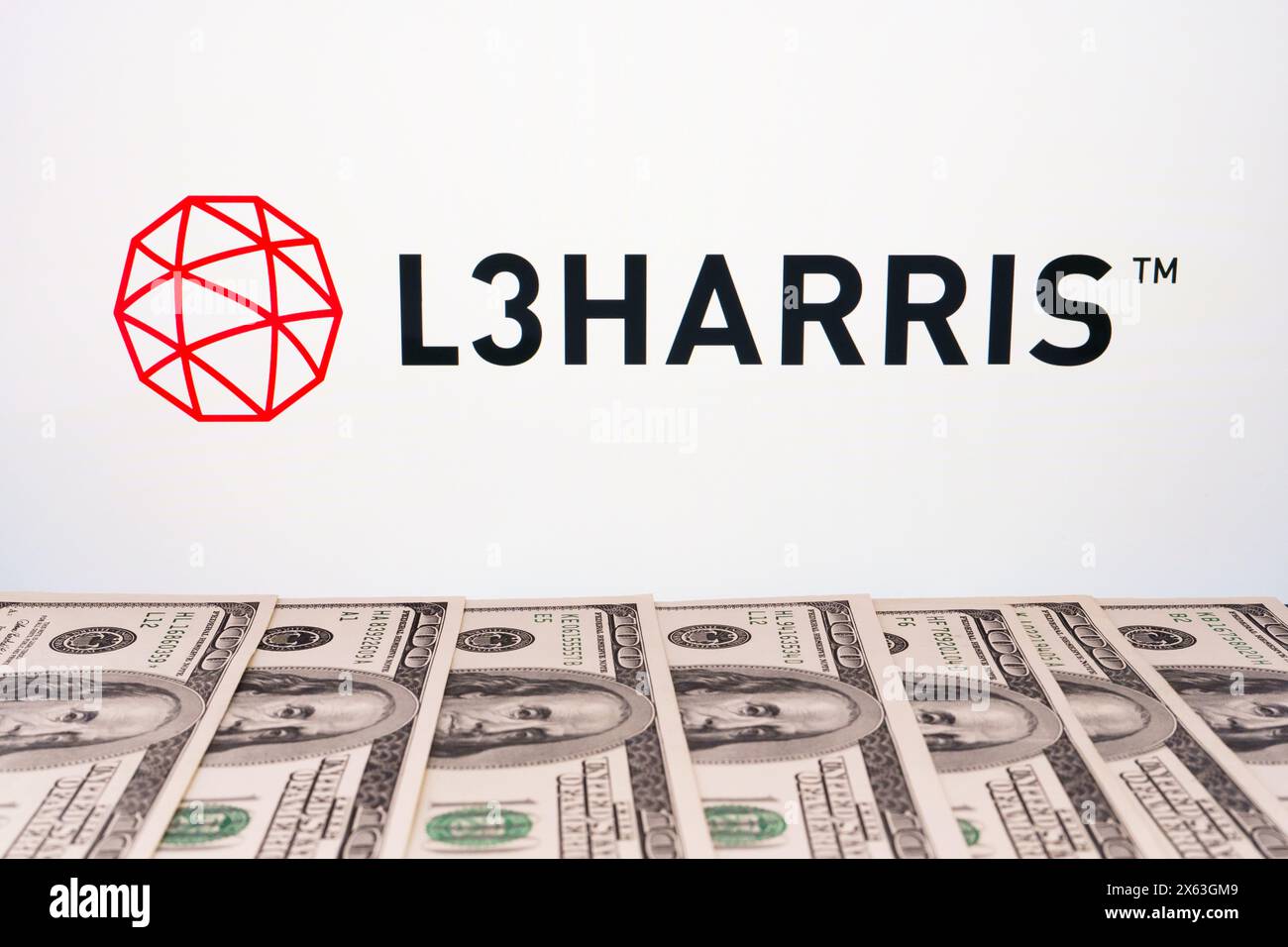 Logo L3HARRIS visto sullo schermo e banconote in dollari americani davanti ad esso. Stafford, Regno Unito, 28 aprile 2024 Foto Stock