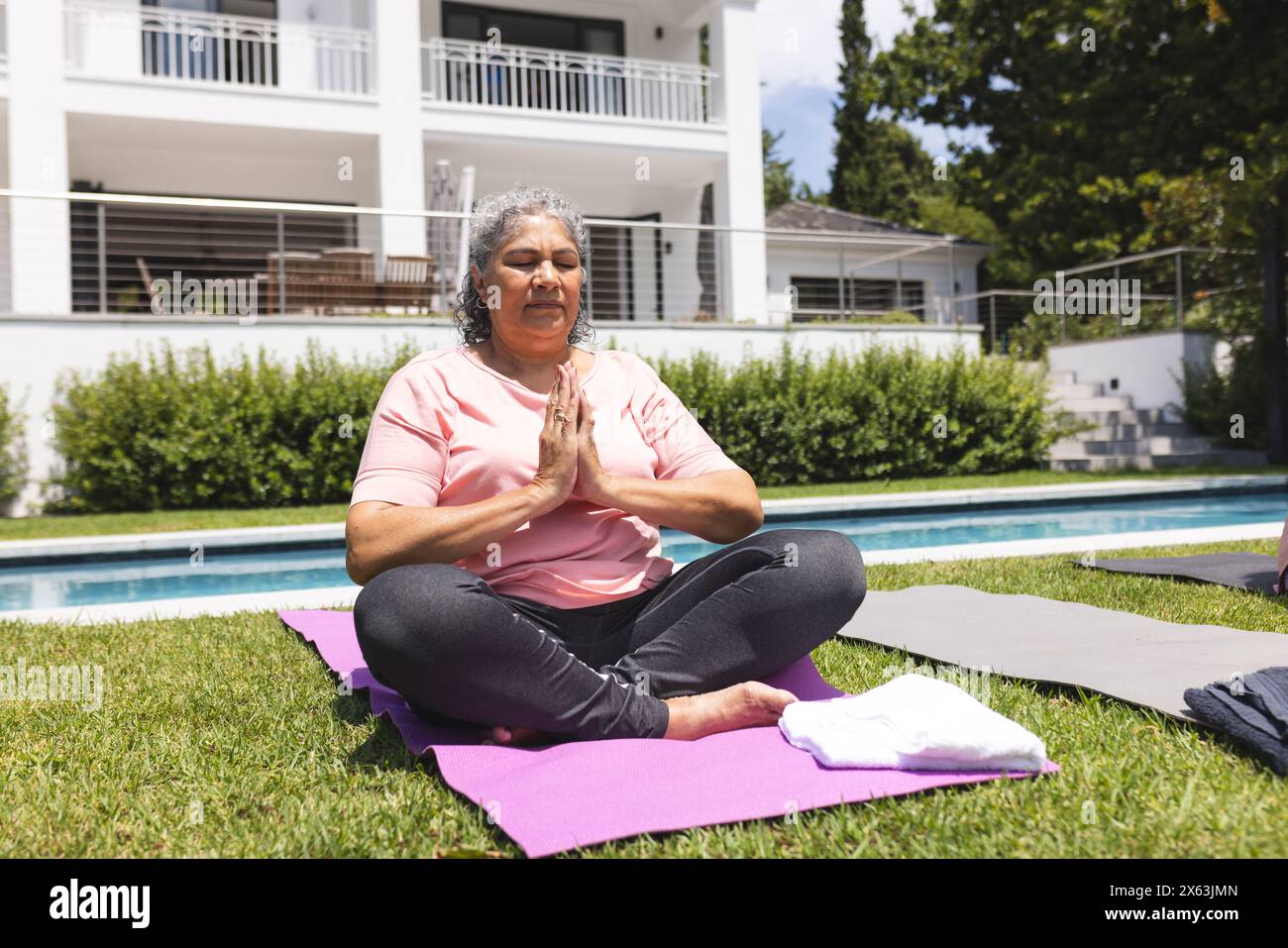 All'aperto, donna birazziale anziana seduta a gambe incrociate su un tappetino per yoga, meditando Foto Stock