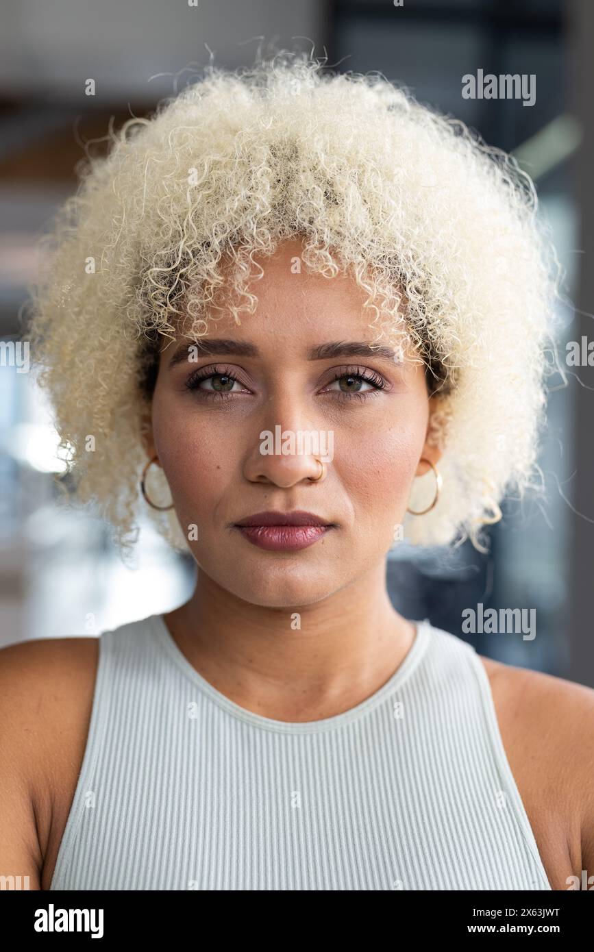 In un ufficio moderno, giovane donna birazziale con capelli biondi ricci in piedi da sola Foto Stock