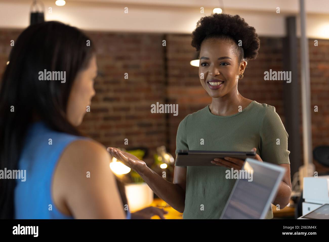 In ufficio, diverse colleghe di lavoro condividono un tablet, sorridendo insieme Foto Stock