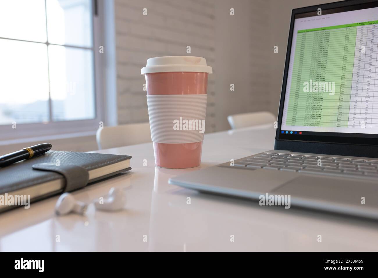 In ufficio, un computer portatile che mostra un foglio di calcolo su una scrivania bianca accanto alla tazza da caffè rosa Foto Stock