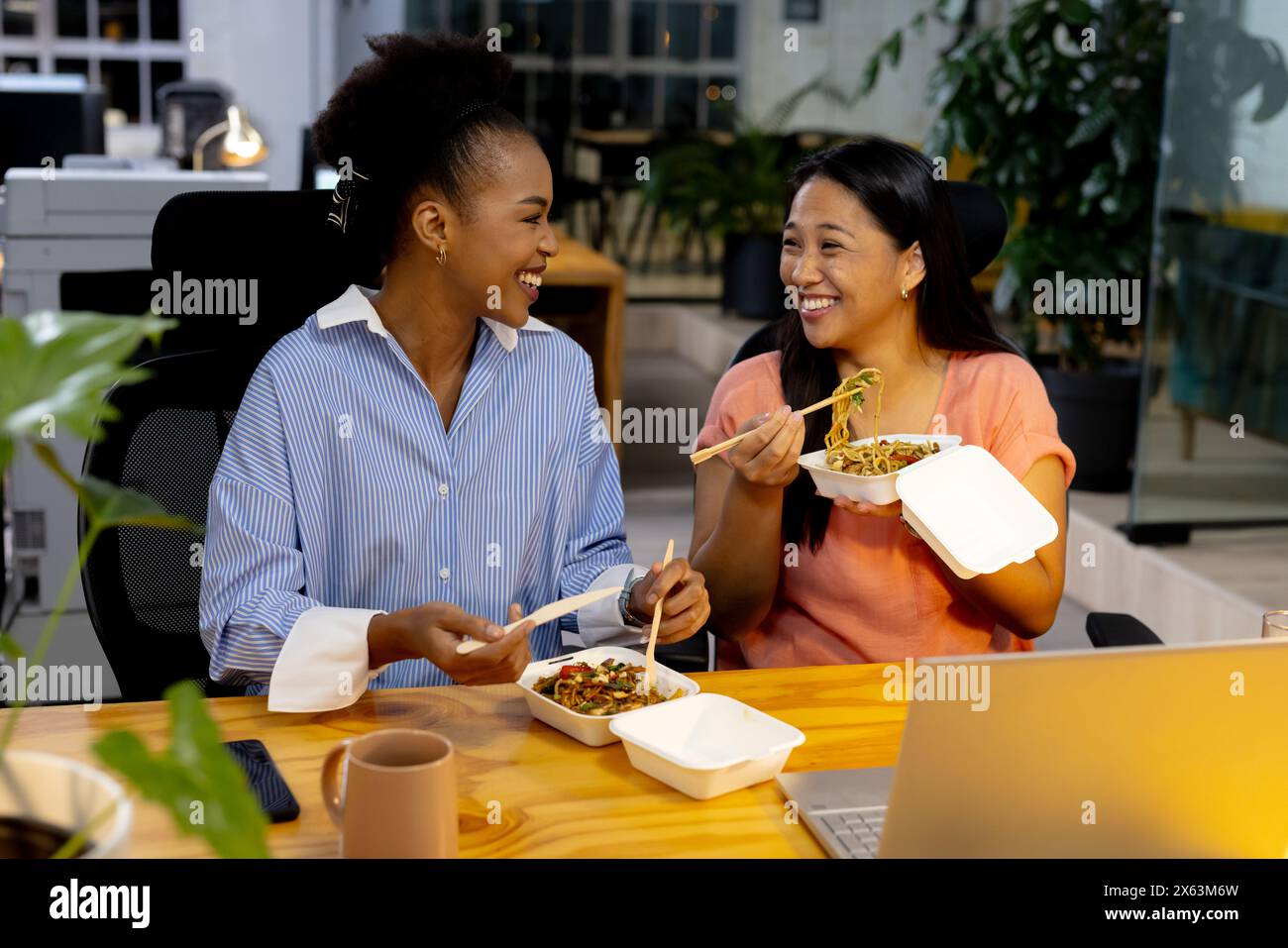 Diverse colleghe si godono un pasto e lavorano fino a tardi in ufficio Foto Stock