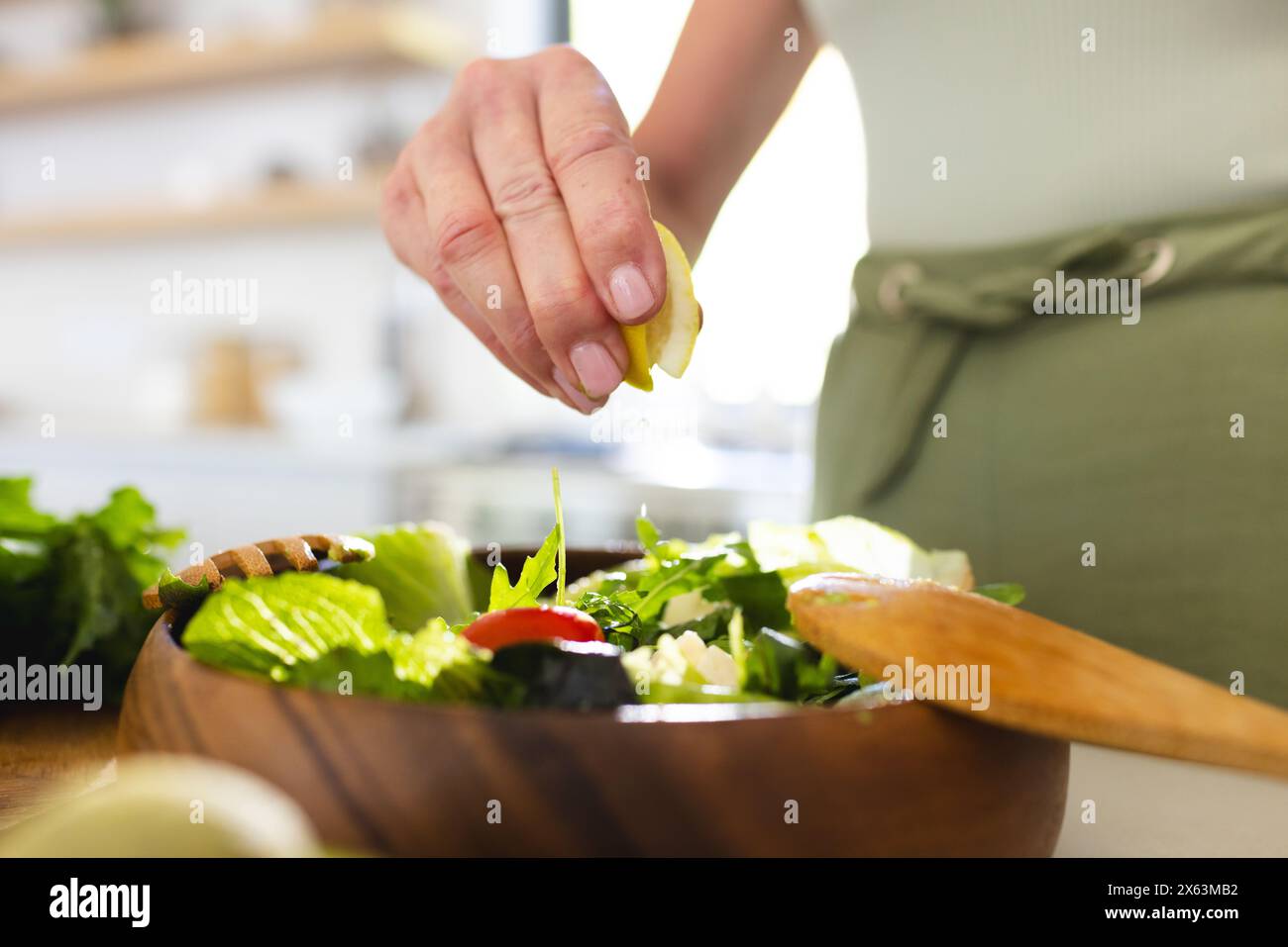 A casa, una donna caucasica matura che spreme il succo di limone sull'insalata Foto Stock