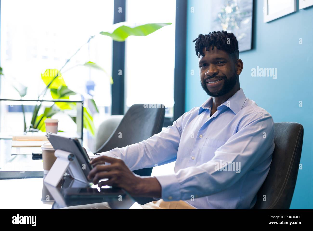 Uomo afroamericano di mezza età che tiene un tablet, sorride alla macchina fotografica in ufficio Foto Stock