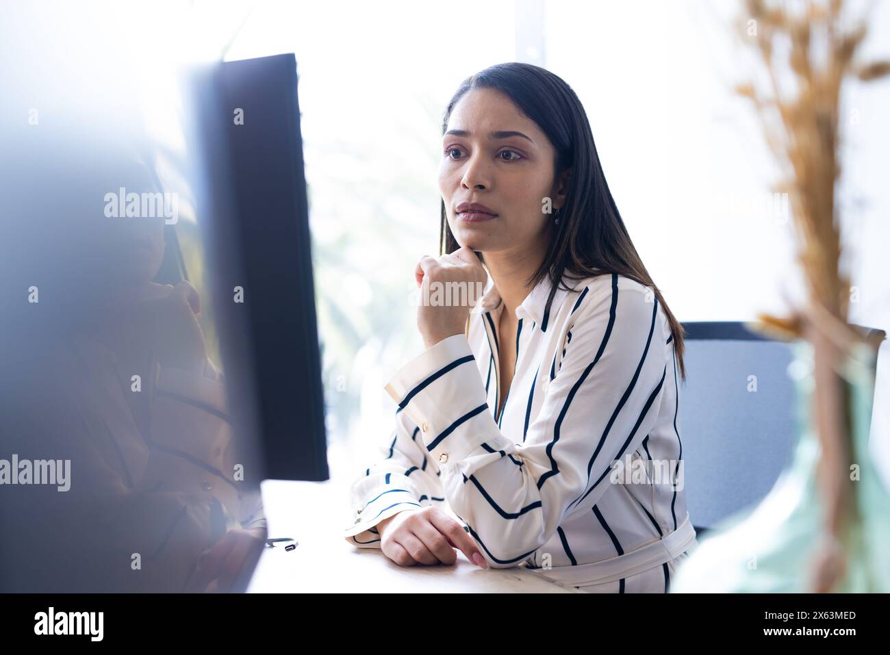 Donna birazziale di mezza età si concentra sullo schermo del computer, sulla camicia a righe, in ufficio Foto Stock