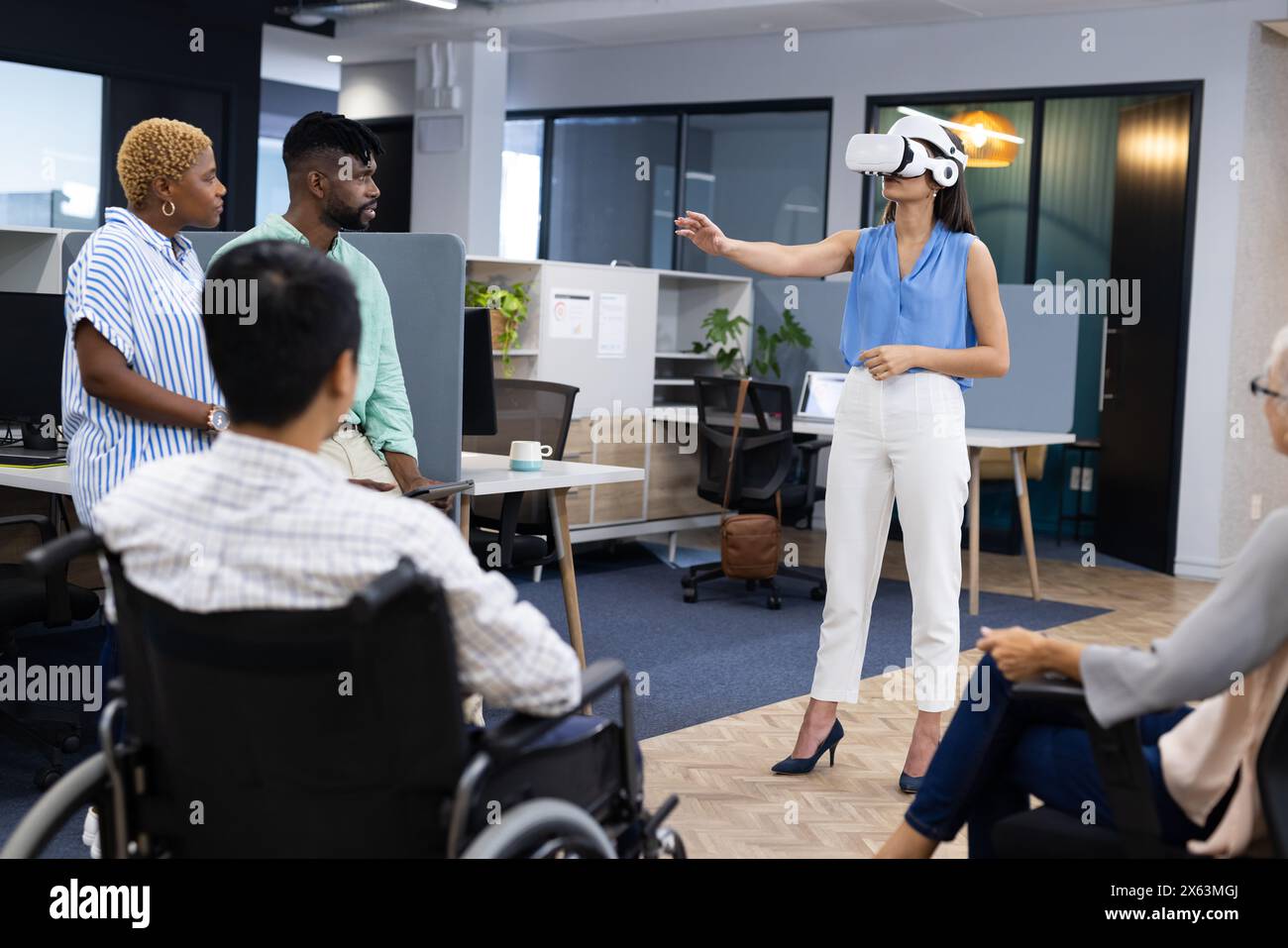 In ufficio, un team eterogeneo che ascolta donne caucasiche con il visore VR che punta Foto Stock