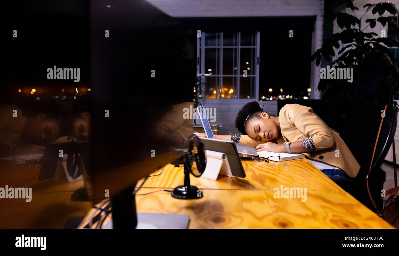 Una donna d'affari afroamericana riposa, apparendo stanca alla scrivania del suo ufficio Foto Stock