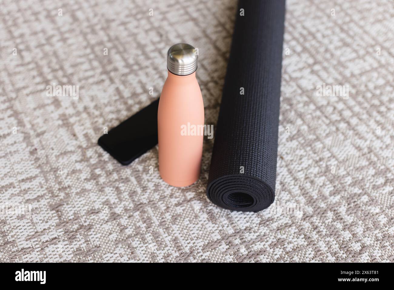 A casa, tappetino nero per yoga arrotolato, bottiglia d'acqua di pesca sul pavimento testurizzato Foto Stock