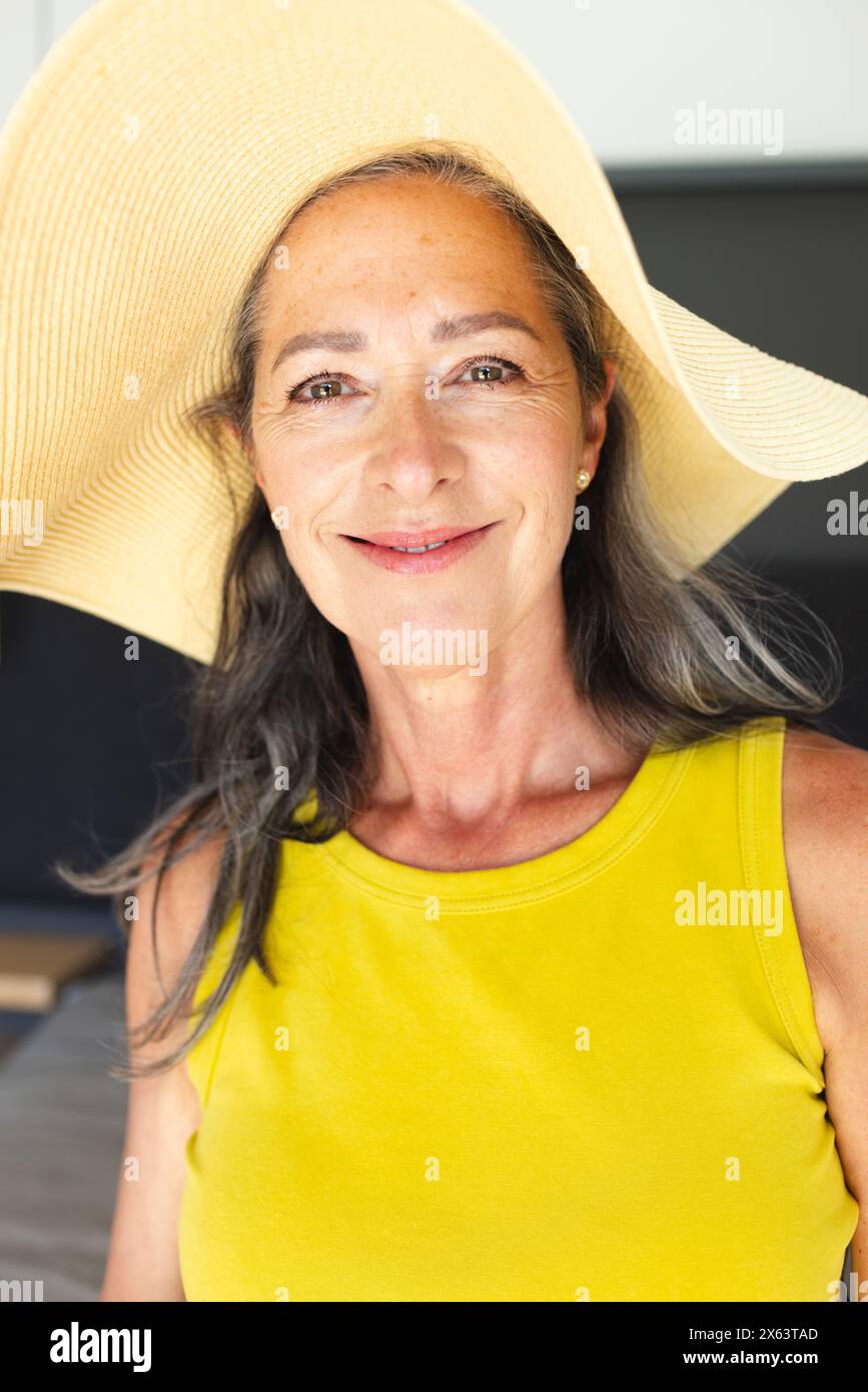 A casa, donna caucasica matura che indossa un grande cappello da sole e una maglietta gialla, sorridendo dolcemente Foto Stock