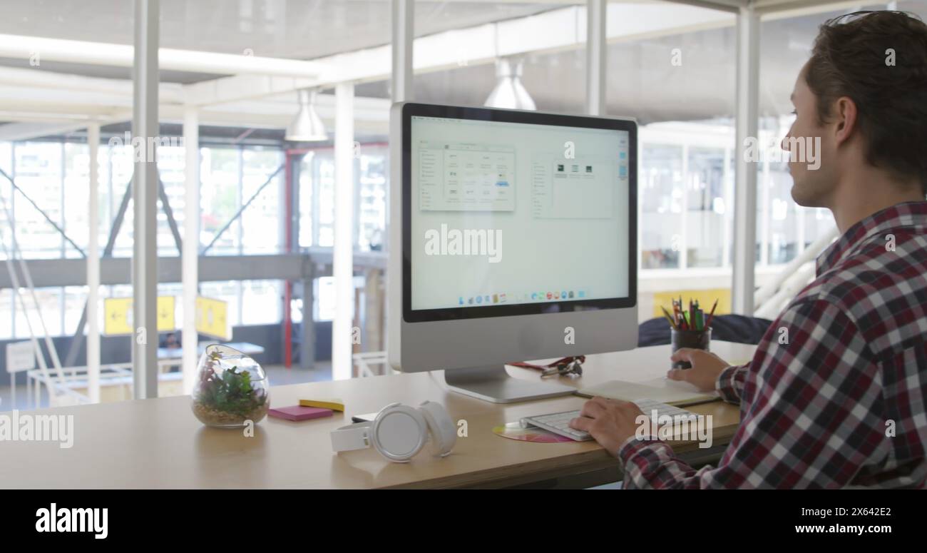 Immagine di un collega maschio caucasico, che indossa una camicia a quadri, che studia un grande schermo Foto Stock