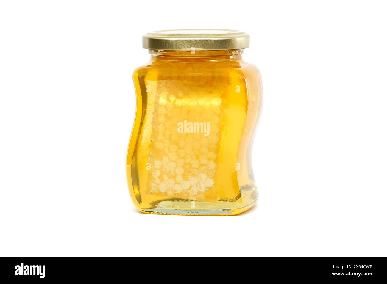 Un vaso di vetro con coperchio dorato contiene miele con favo riempito quasi fino in cima, su sfondo bianco Foto Stock