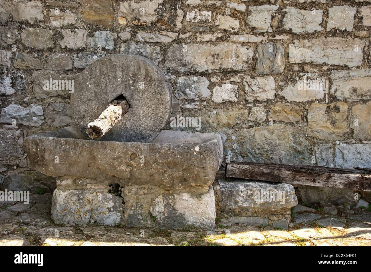 Antico mulino in pietra contro il muro di pietra Foto Stock